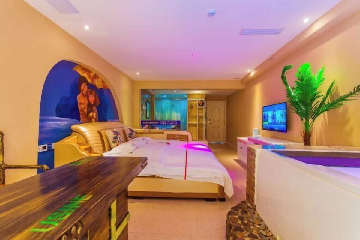 Una habitación de hotel moderna con una cama, un escritorio, un televisor y una planta grande.