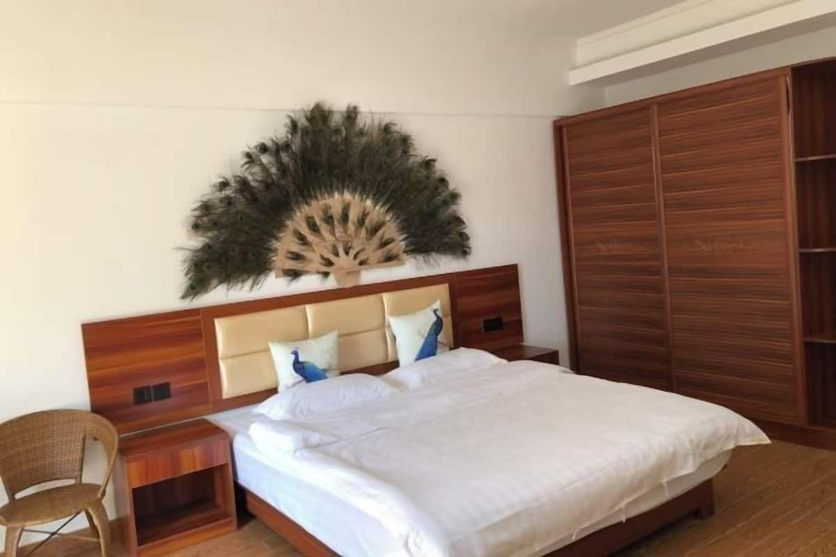 Un dormitorio con cabecera de madera, una cama grande con ropa de cama blanca, una mesita de noche de madera, una silla de mimbre y un armario de madera.