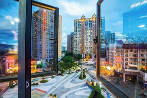 Un edificio de gran altura con varios pisos, un amplio frente de vidrio y vistas de un paisaje urbano con otros edificios y una carretera.