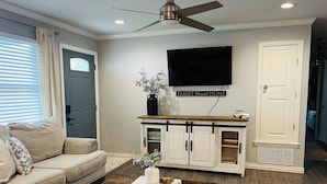 A living room with a sofa, coffee table, and TV mounted on the wall. - Adversity Home - Open Concept, with Pacman Machine. Close to I-40 Airport (Amarillo)