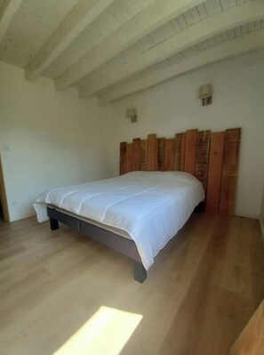 Quarto com cabeceira de madeira, colcha branca e chão de madeira.