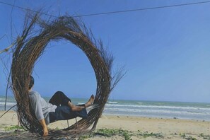 Una persona sentada en una estructura circular de mimbre en una playa, con el océano al fondo.