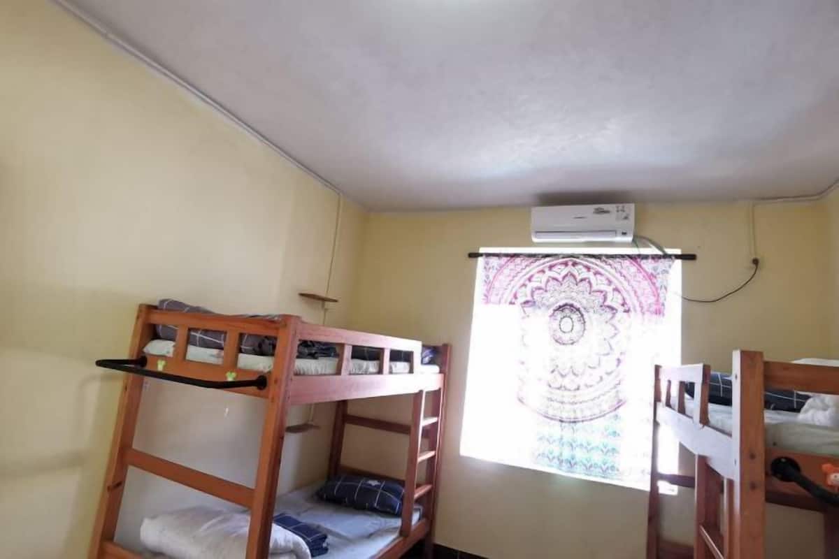 Een studentenkamer met stapelbedden, een raam met een decoratief gordijn en een airconditioner.