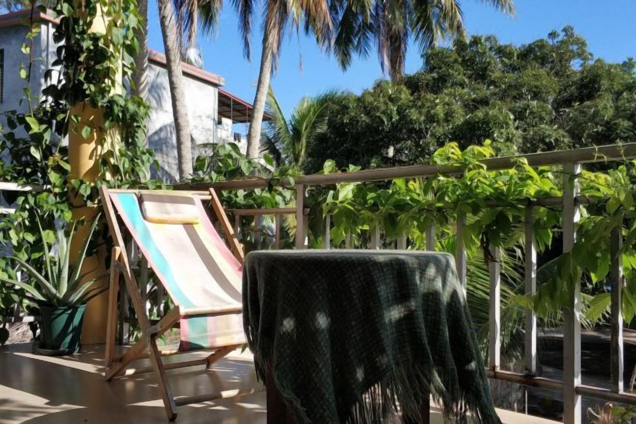 A balcony with a table, a folding chair, and a view of a garden with various plants.