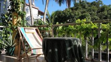 A balcony with a table, a folding chair, and a view of a garden with various plants.
