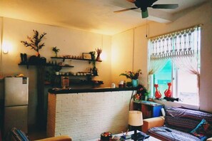 Un espacio habitable compacto con kitchenette, un sofá y una ventana con cortinas.
