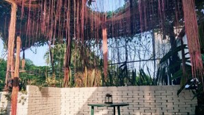 Une terrasse en bois avec un mur de briques, une petite table sur laquelle est posée une lanterne, et des plantes grimpantes suspendues.