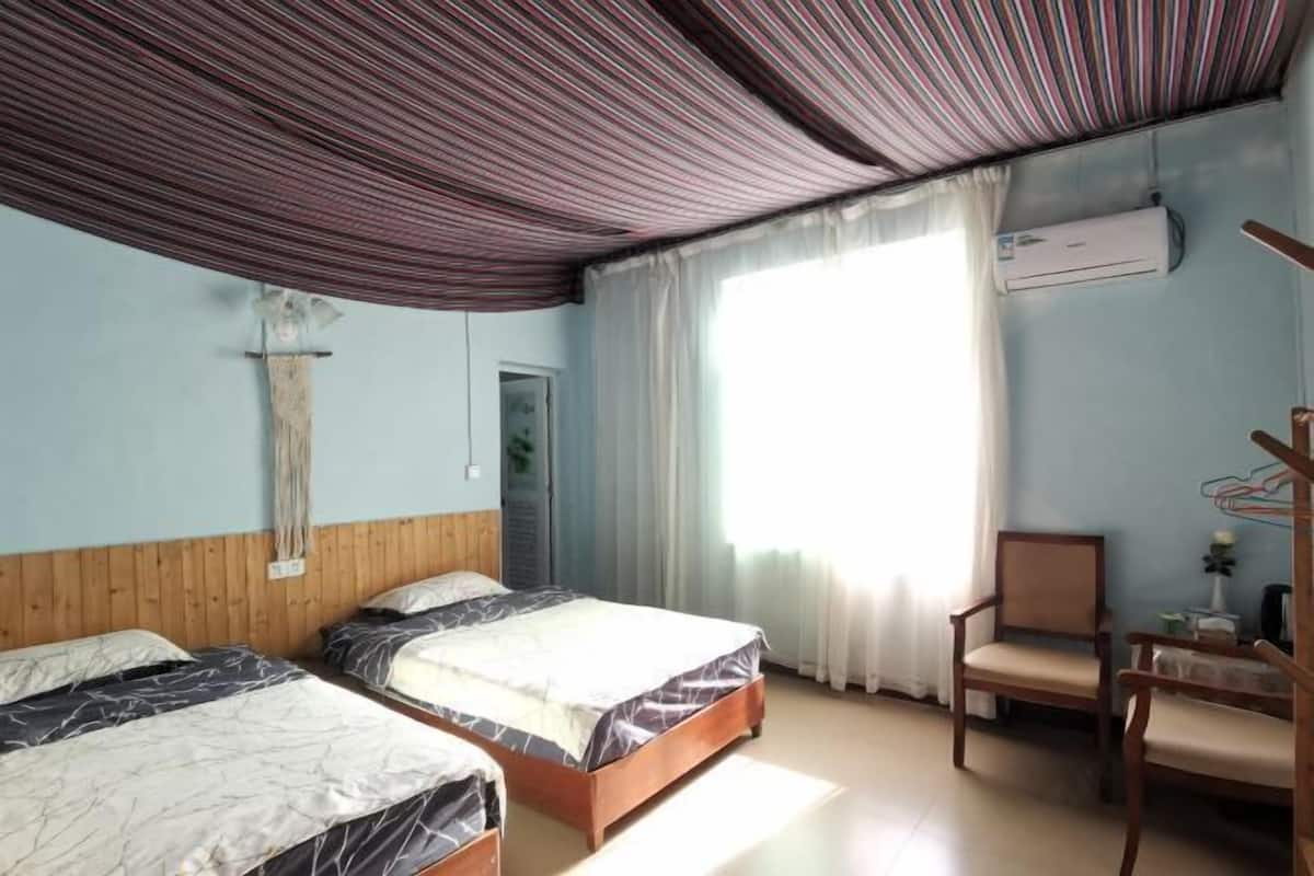 Hotelkamer met twee bedden, een houten hoofdbord, een stoel, een airconditioning en een raam met gordijnen.