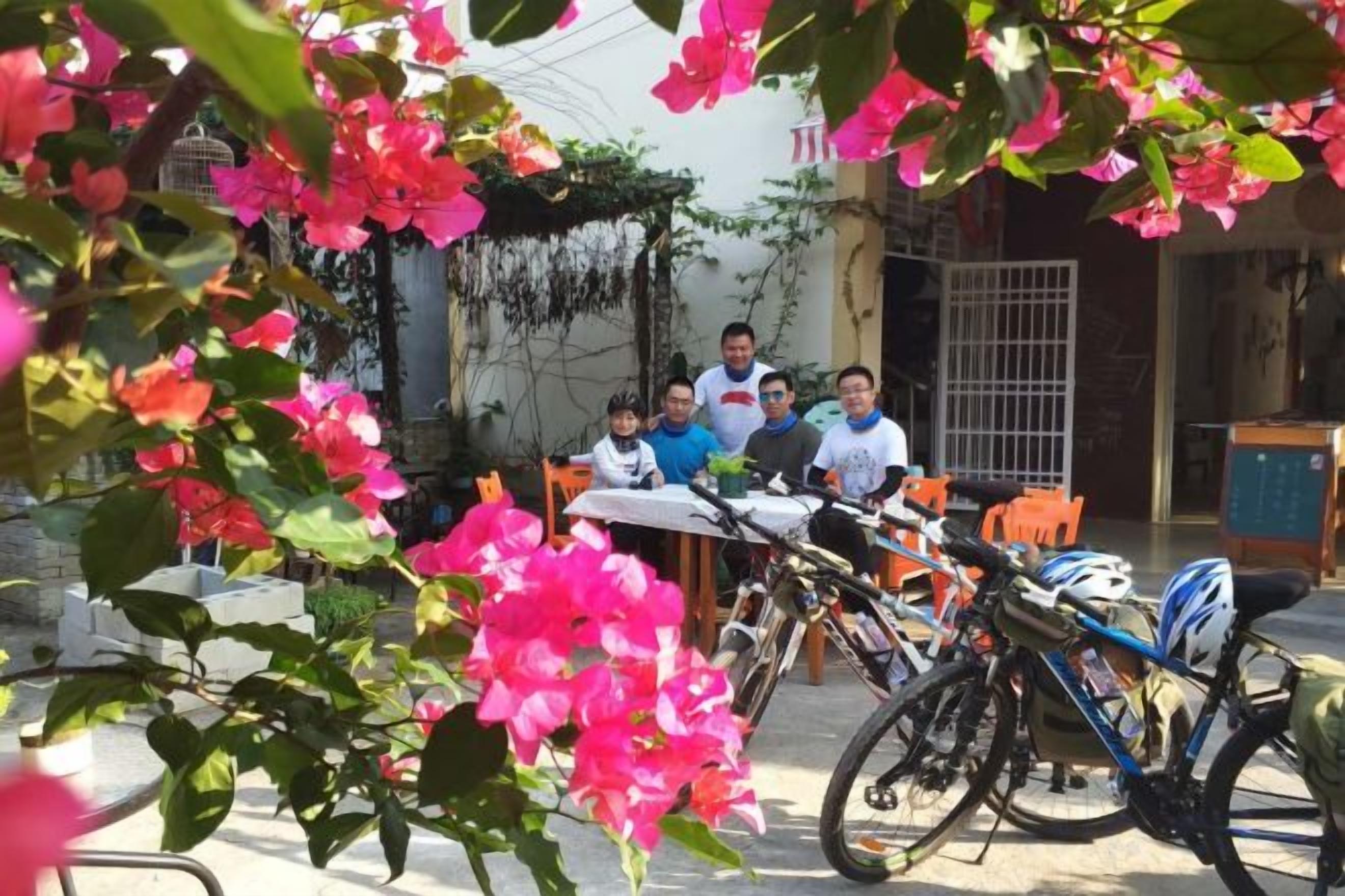 A group of people seated at a table outdoors with bicycles parked nearby.