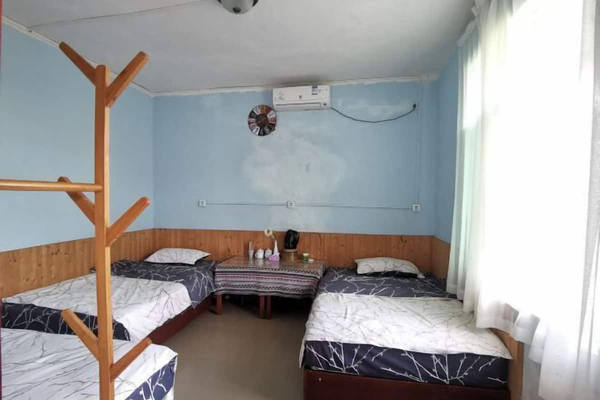 Een kamer met twee bedden, een houten ladder, een klein tafeltje met een klok en een wandairconditioner.