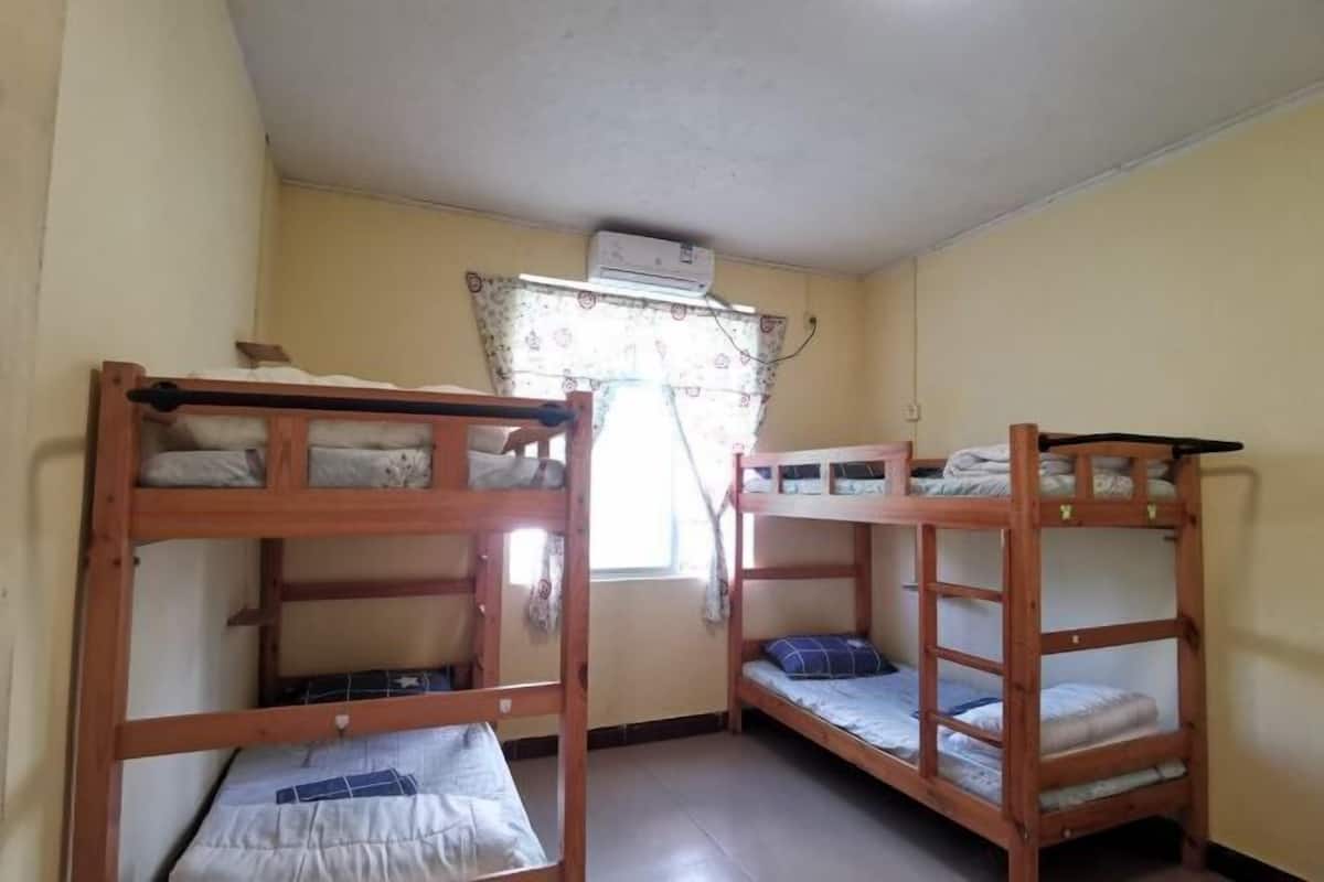 Een studentenkamer met stapelbedden, een raam met gordijnen en een airconditioning.