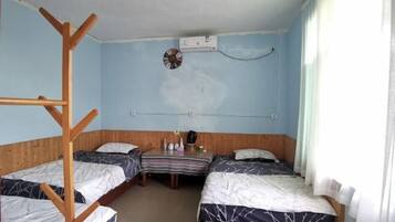 Een kamer met twee bedden, een houten trap, een airconditioning, een klein tafeltje met een klok en een raam met gordijnen.