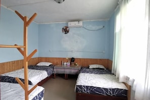 Une chambre avec deux lits, une échelle en bois, un climatiseur, une petite table avec une horloge et une fenêtre avec des rideaux.