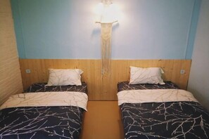 Une chambre avec deux lits, chacun recouvert d’une couvre-lit à motifs et agrémenté d’oreillers blancs. Un luminaire est fixé au mur, au-dessus des lits.