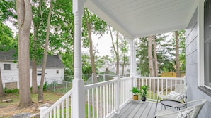 A covered porch with white railings, two wicker chairs, and a small table.
