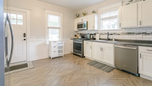 A modern kitchen with white cabinetry, stainless steel appliances, and a herringbone wood floor.