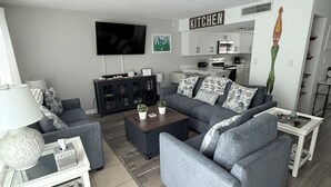 A modern living room with grey sofas, a coffee table, a TV, and a kitchen area.