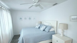 A bedroom with a bed, a nightstand, a ceiling fan, and a window with curtains.
