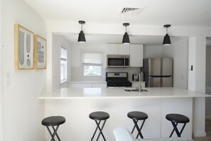 A modern kitchen with white cabinetry, stainless steel appliances, and black bar stools.