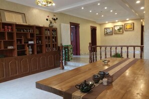 A spacious room with a wooden table, shelves with books and decorative items, a chandelier, and framed pictures on the wall. - Pulu Inn (Dalian)