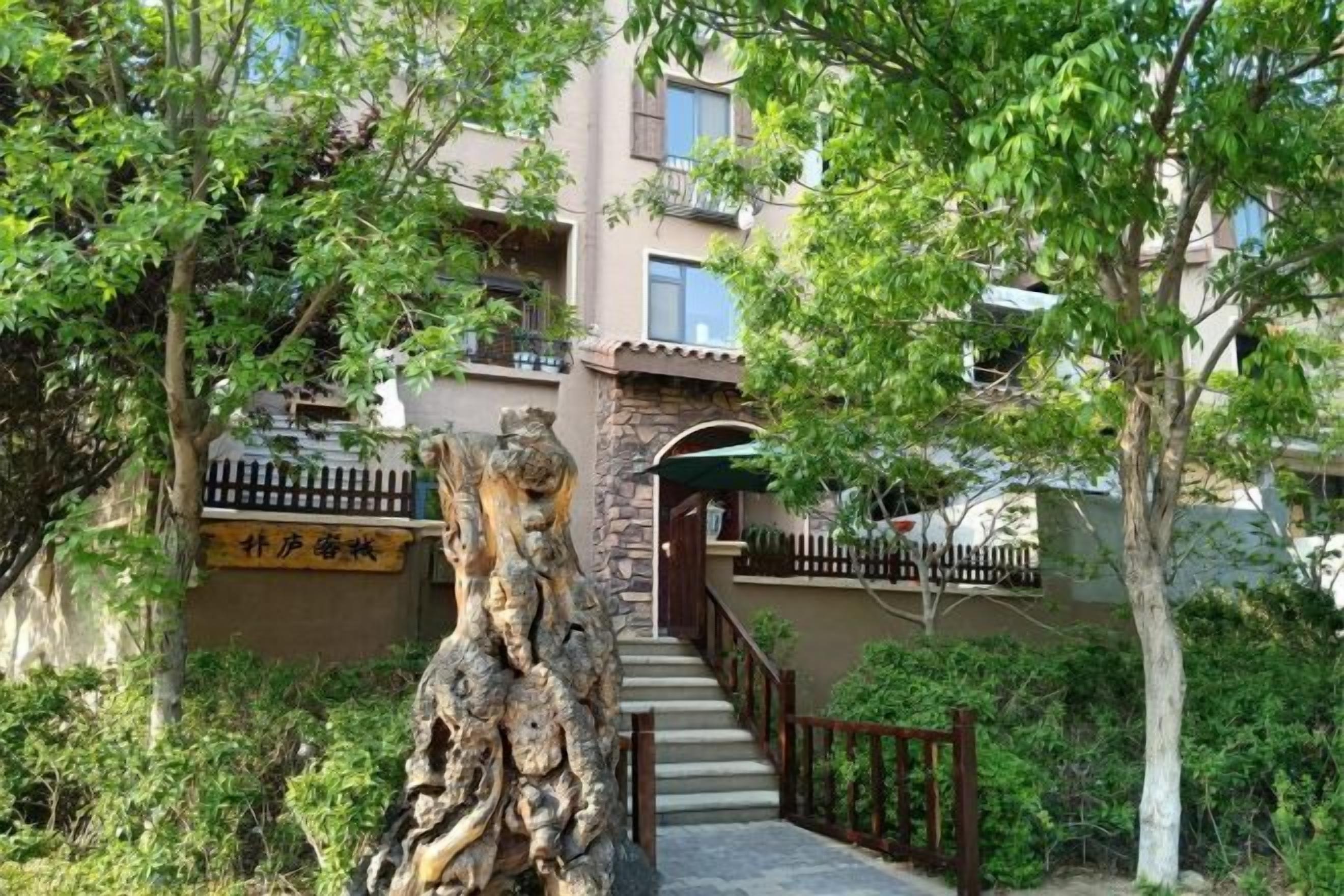 A building with a stone staircase leading to a door, surrounded by greenery and a fence.