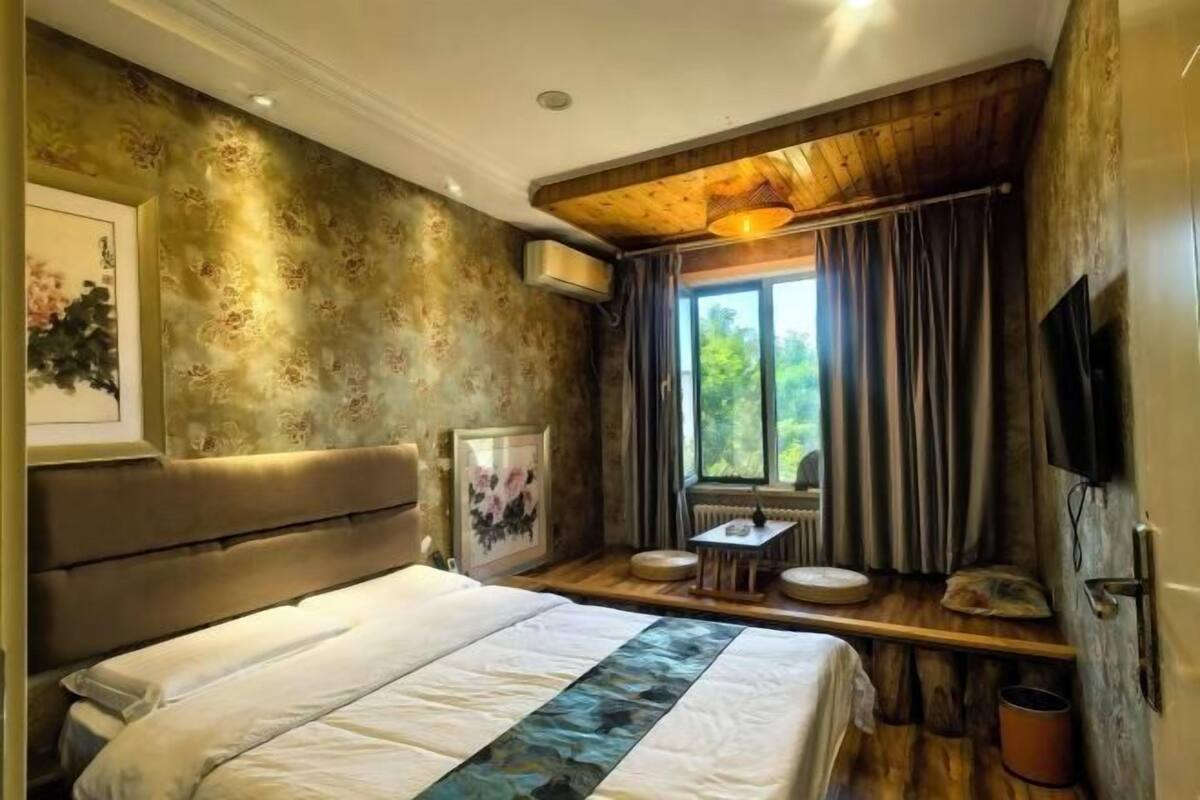 Un dormitorio con una cama grande, una mesita, una ventana con cortinas y techo de madera.