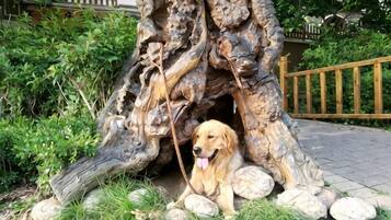 A dog sitting in front of a large, naturalistic tree sculpture with rocks around it.