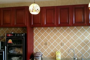 Una cocina con armarios de madera, microondas, hervidor y lámpara colgante.