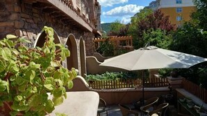 En terrasse med udendørs møbler, stor parasol og en bygning med hvælvinger.