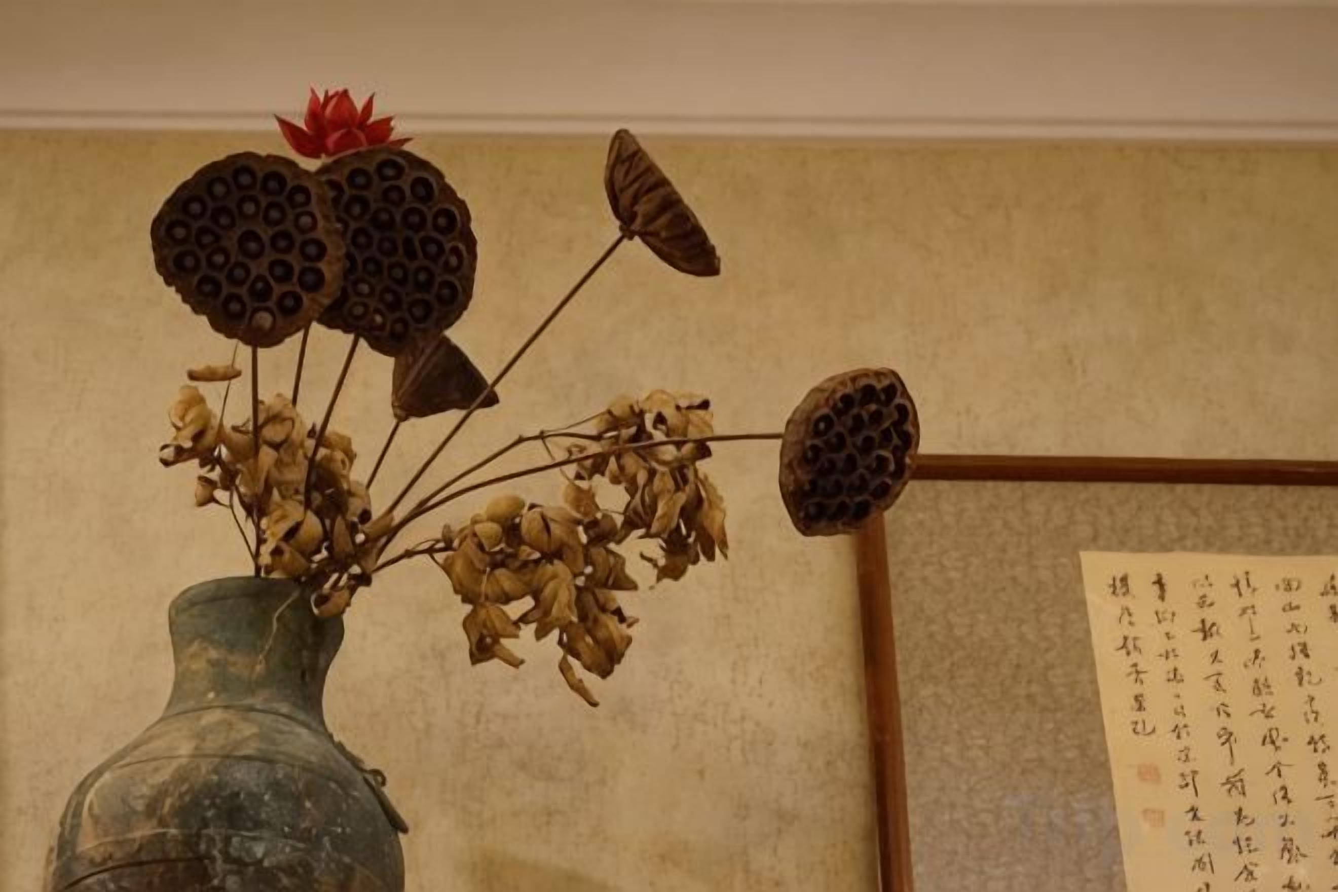 Un vaso con fiori secchi e foglie, una parete con calligrafia e una cornice di legno.