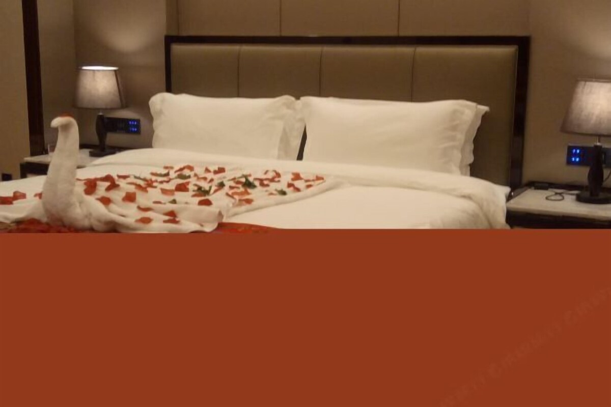 A hotel room with a bed, white bedding, a nightstand with a lamp, and a digital clock.