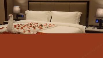 A hotel room with a bed, white bedding, a nightstand with a lamp, and a digital clock.