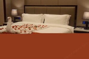 A hotel room with a bed, white bedding, a nightstand with a lamp, and a digital clock. - Jinhengsheng Holiday Hotel (Yunxiao)