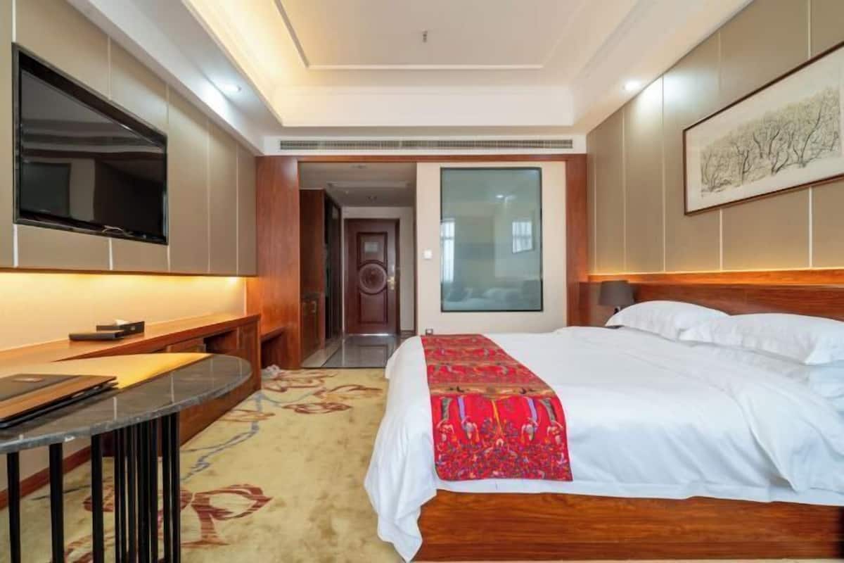 A hotel room with a bed, a TV, a desk, and a door leading to another room.