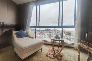 A room with a sofa, a small round table, and a view of a cityscape through large windows. - Jinhengsheng Holiday Hotel (Yunxiao)