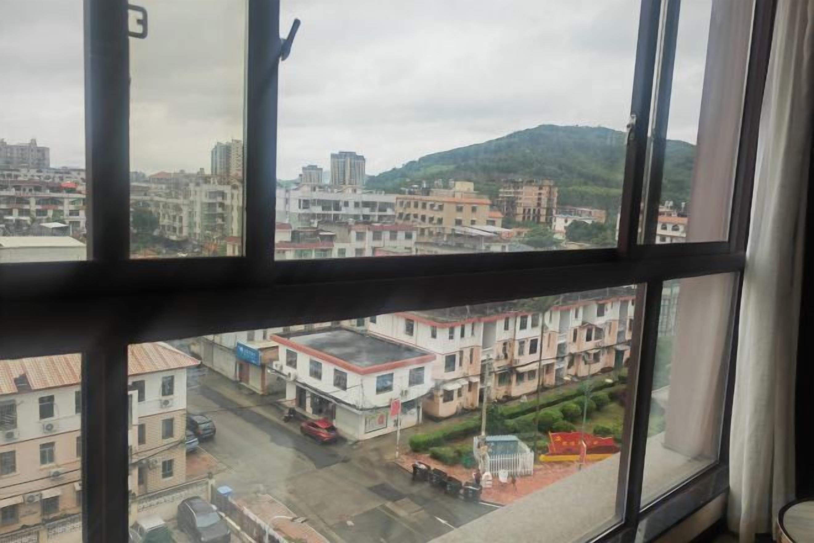 A view through a window of a cityscape with buildings, a road, and a hill in the background.
