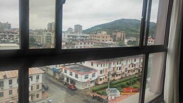 A view through a window of a cityscape with buildings, a road, and a hill in the background.