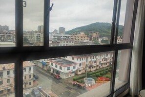 A view through a window of a cityscape with buildings, a road, and a hill in the background. - Jinhengsheng Holiday Hotel (Yunxiao)
