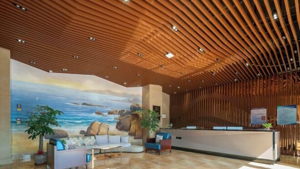 A modern reception area with a wooden ceiling, a mural of a beach scene, and a reception desk.