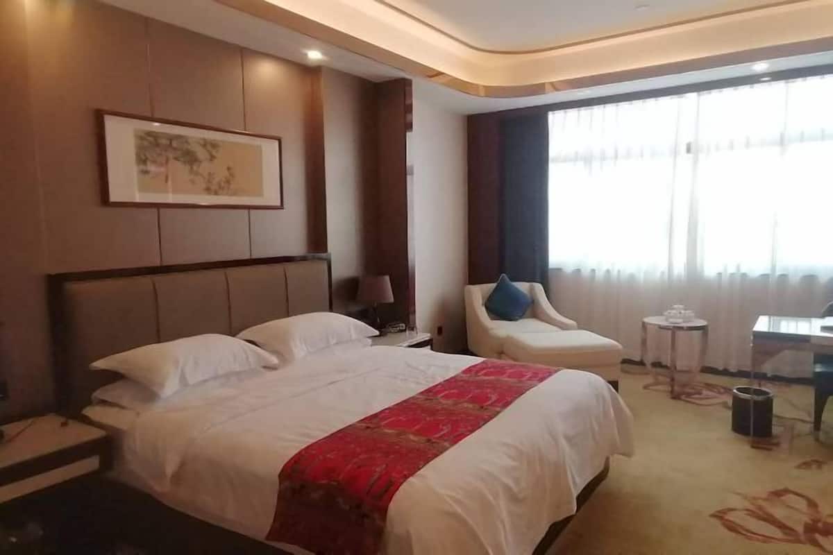 A hotel room with a large bed, a chair, a small table, and a window with curtains.
