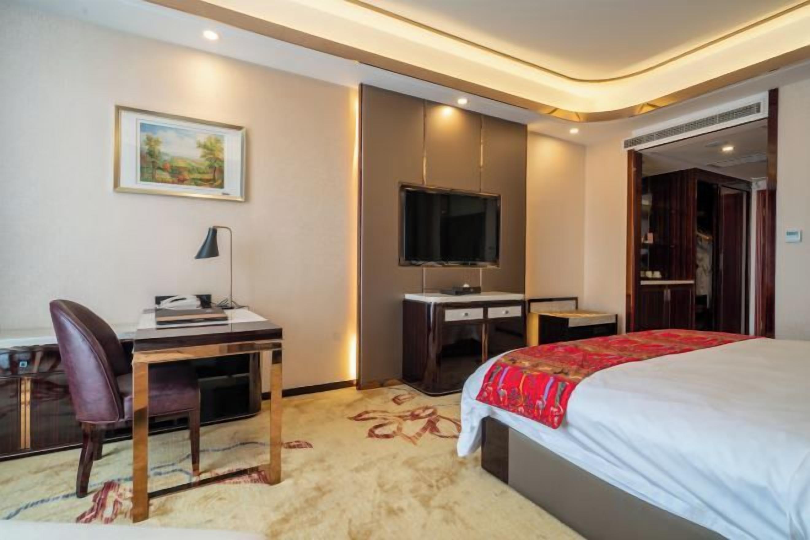 Habitación de hotel con cama, escritorio, silla, televisión y piso alfombrado.