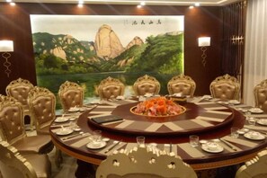 A conference room with a round table, chairs, and a large painting of a mountainous landscape. - Jinhengsheng Holiday Hotel (Yunxiao)