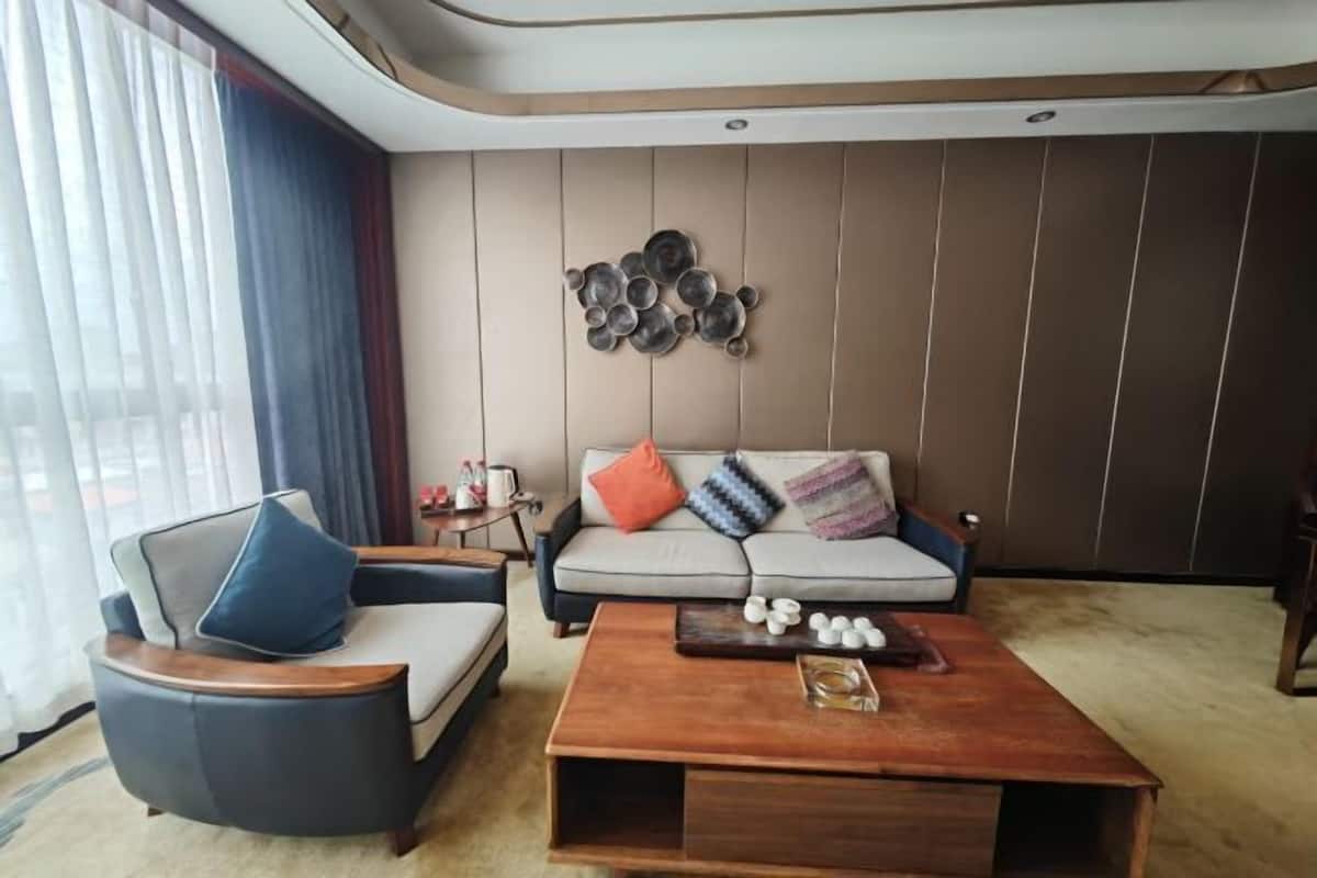 A modern living room with a sofa, armchair, and coffee table, a wall art piece, and a window with curtains.