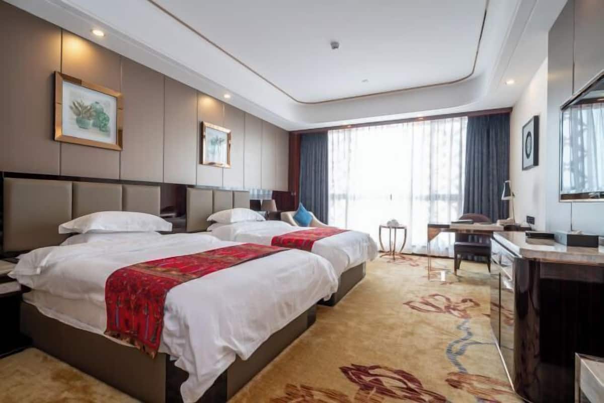 A hotel room with two beds, a desk, a chair, and a large window.