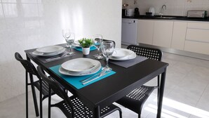 A dining table set with plates, glasses, and cutlery in a modern kitchen with white cabinets and a dishwasher. - 2 Bedroom Apartment in Portimão (Portimão)