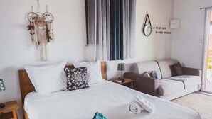 Habitación de hotel con una cama de madera, un sofá, un ventilador de techo y un aire acondicionado instalado en la pared.