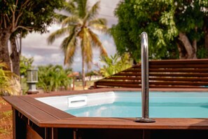 A wooden poolside with a metal pole, surrounded by palm trees and a wooden deck. - Julien Caraïbes • Domaine de Meilly (Saint-Louis)