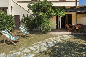 A patio with two striped lounge chairs, a table with chairs, and a stone pathway leading to a building entrance.