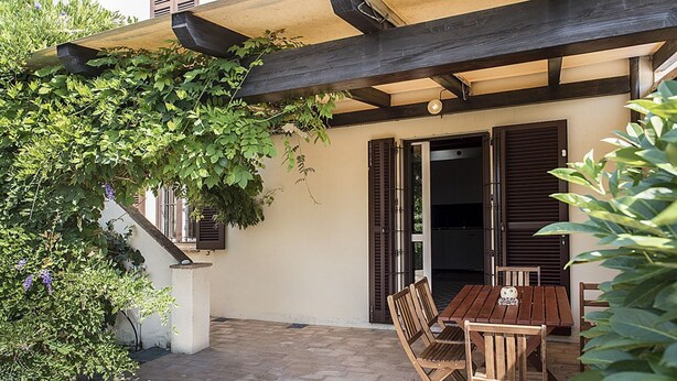 A patio area with a wooden table and chairs, a covered seating area, and a staircase with wooden railings. - N256 - Numana, brand new three-room apartment with garden (Sirolo)
