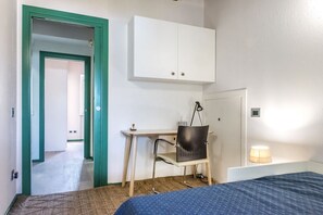 A bedroom with a bed, a desk with a chair, a wardrobe, and a lamp.